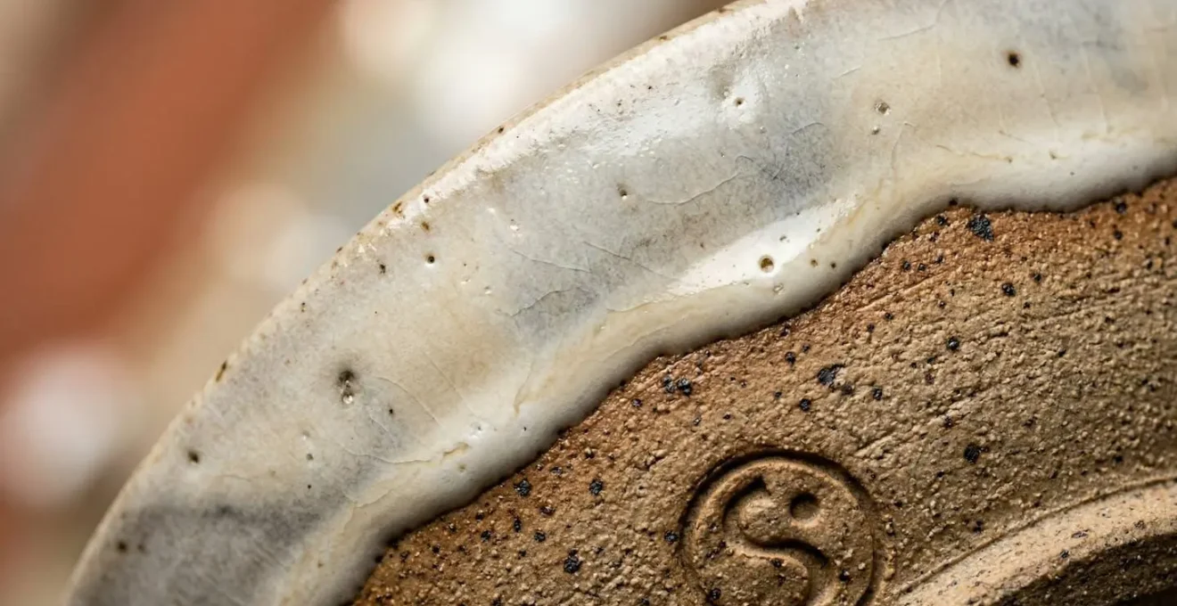 Vue macro d'une céramique artisanale montrant les variations naturelles de l'émail et la signature du potier